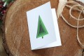 Otwierana świąteczna kartka firmowa z minimalistyczną zieloną choinką z efektem wyciętego papieru oraz gwiazdkami i życzeniami w środku