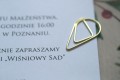 Elegancki złoty spinacz, pod nim zaproszenie oraz kalka