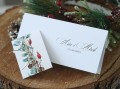Świąteczne zaproszenie ślubne z zimowymi gałązkami, obok ozdobna obwoluta z lnianym sznureczkiem